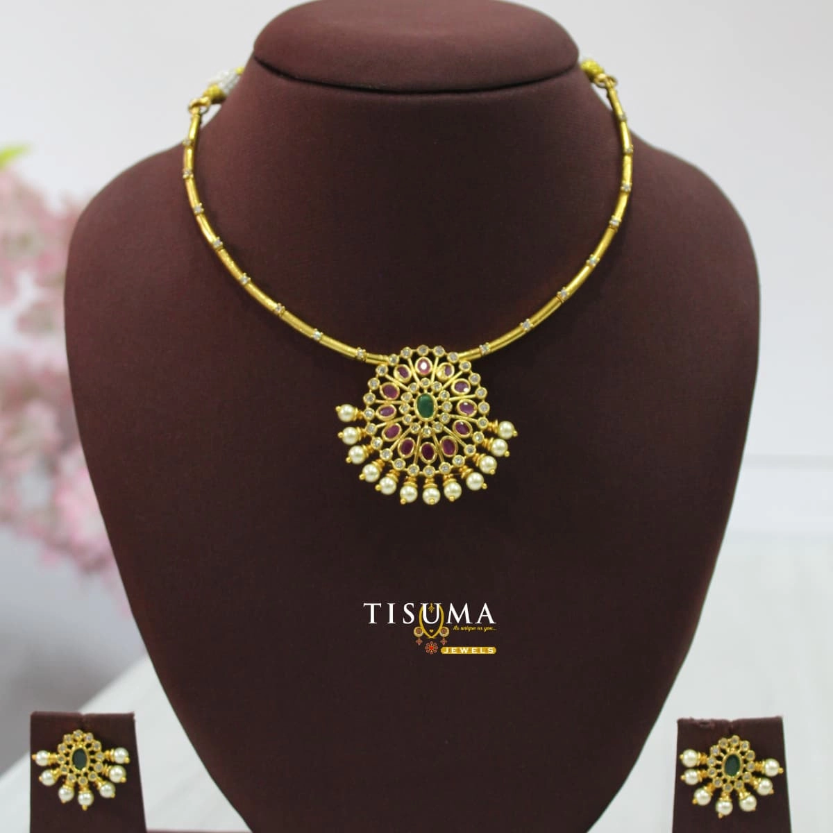 Traditional gold-finish pendant necklace set with ruby and green colour stones, pearl drops, and matching earrings | Tisuma Jewels