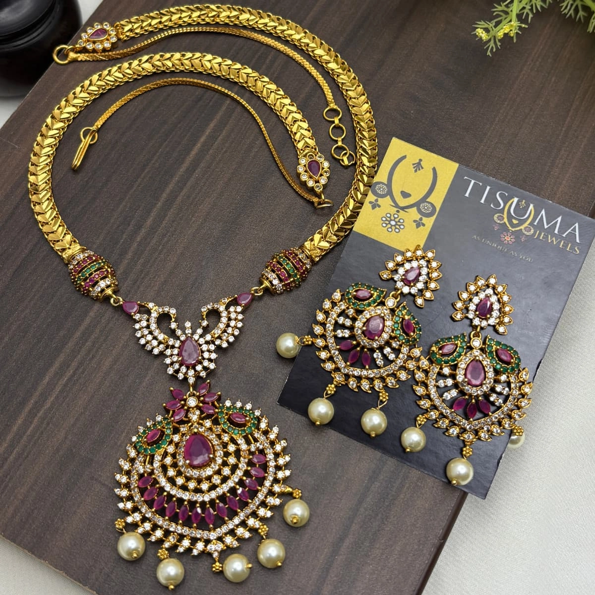 Gold-plated traditional haram necklace set with ruby and green stones, pearl drops, and matching statement earrings by Tisuma Jewels.