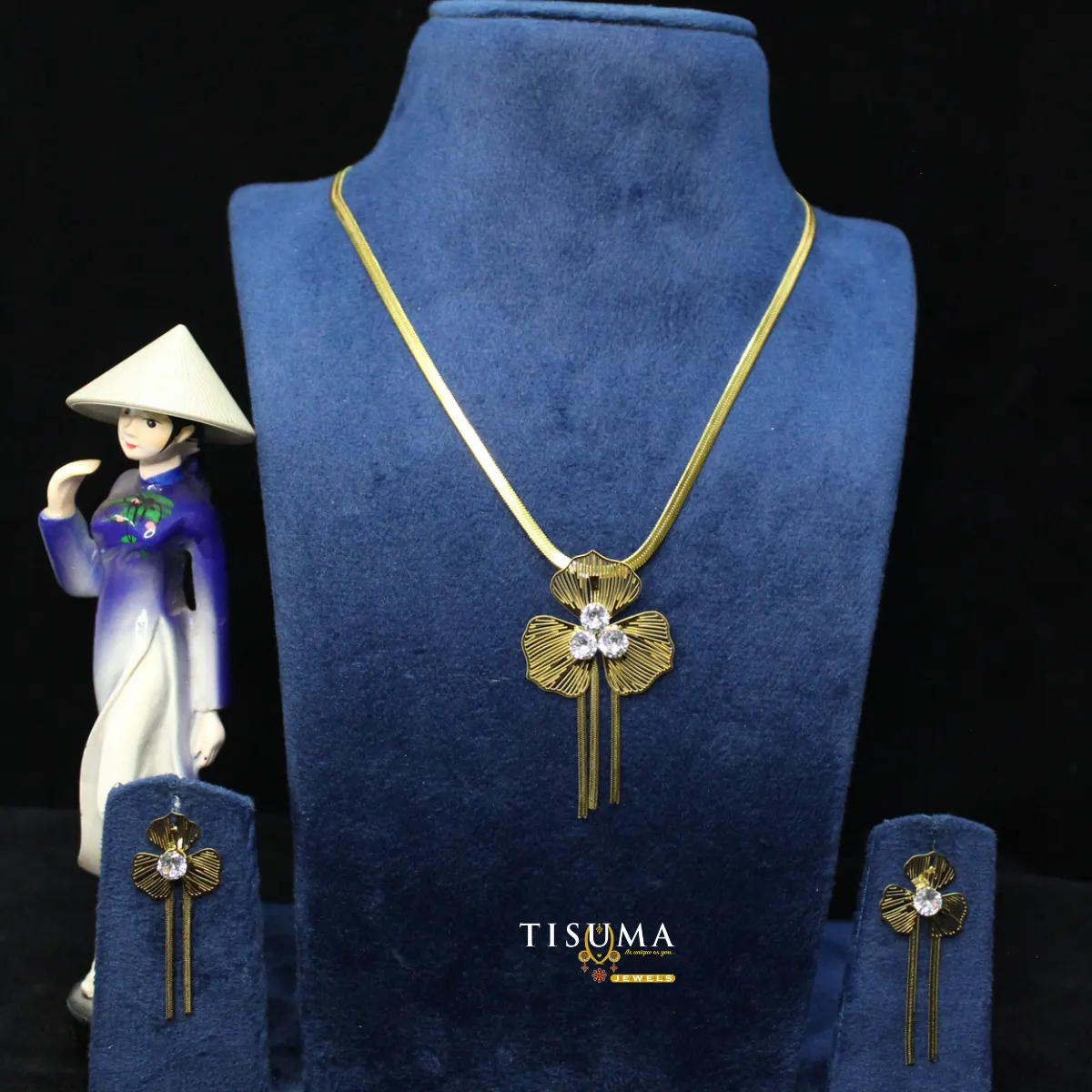 TISUMA gold-tone floral pendant necklace and matching crystal drop earrings set displayed on a blue jewellery bust